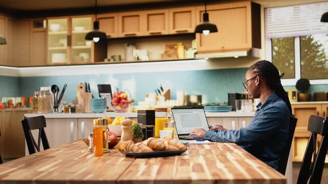 Black IT engineer works remotely coding on laptop and terminal windows at home, using database management for high-tech digital engineering and development.