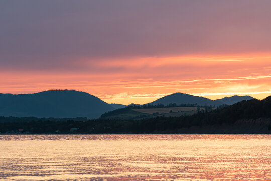 Gaspesie, Canada, 20 August 2026 : Vibrant sunset sky reflects on calm lake water with dark hills in silhouette
