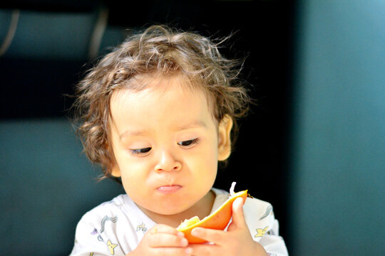 Cute toddler eating the quarter of orange.