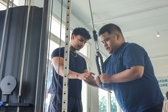 Personal Trainer Instructing Client During Triceps Cable Pushdown Workout in Modern Gym Facility