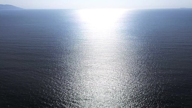 Magnificent sea horizon view during sunrise with bright sun glare reflecting on calm blue water surface as drone moves forward in peaceful clear sky environment