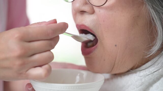 訪問介護で高齢者の食事介助をするホームヘルパー、在宅介護、食事支援、食べることをサポートする女性介護職のイメージの顔無しの口元クローズアップの動画