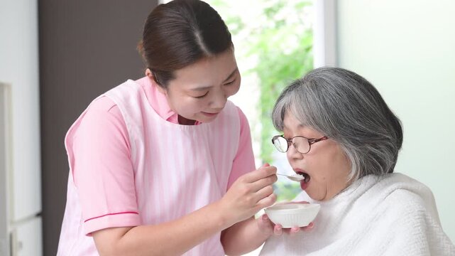 [Slow Motion] A close-up video showcasing a home health aide assisting an elderly person with eating as part of in-home care; home care; meal assistance; and a female caregiver helping someone eat