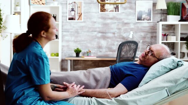 nurse walks toward the bedside and takes a seat near an older man resting with an IV cannula, suggesting attentive nursing care and companionship, also emphasizing reassurance and comfort.