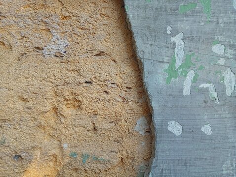 A detailed macro texture of an old weathered concrete plaster wall with peeling green paint layers breaking away to expose a rough yellow porous limestone coquina surface