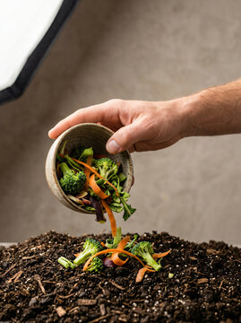 Hand pouring vegetable scraps into a pile of compost for organic gardening.