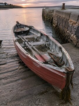 Lapstrake wooden rowboat hauled up a concrete slipway beside a stone quay with oars and grapnel