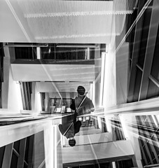 Fototapeta premium Abstract black and white double exposure of a man on escalator in modern building architecture, conceptual symmetrical urban design