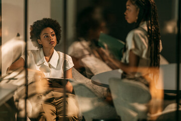 Obraz premium Two businesswomen having conversation through glass office partition at golden hour