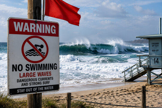 Warning sign reading No Swimming Large Waves with red flag on beach, strong rough ocean waves breaking near lifeguard tower, coastal hazard and beach safety concept
