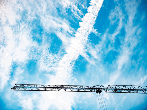 Silhouette of a tall construction crane jib against a blue sky with dramatic cirrus clouds