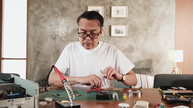 Mature Asian man voltage test at disassembling circuit board with multimeter tool, focusing on precision checks for home electrical appliance DIY fix, electronics component hobby, handyman workshop.