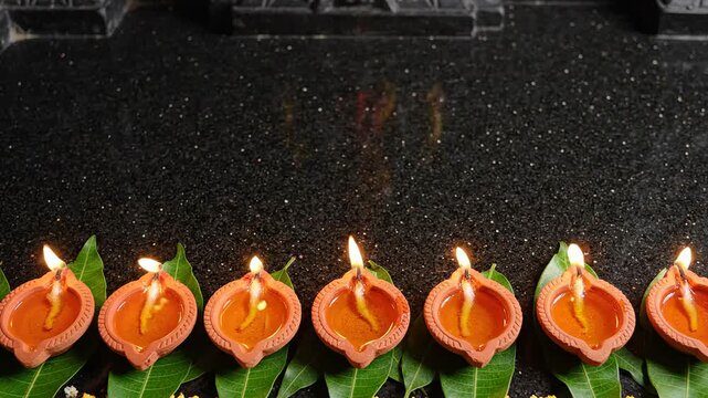 Traditional clay oil lamps glowing brightly on green leaves against a dark background for diwali festival celebration banner with empty copy space for message design