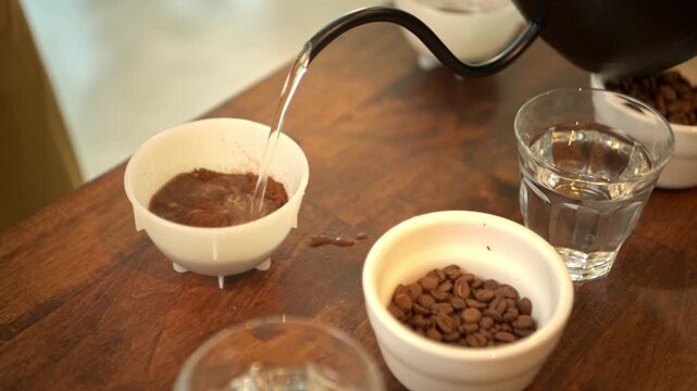 A barista is pouring hot water into a cup containing finely ground coffee beans, preparing it for a Q-Grader to taste