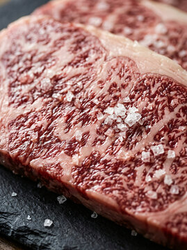 Close up of raw marbled wagyu beef steak with sea salt crystals on a dark stone board.