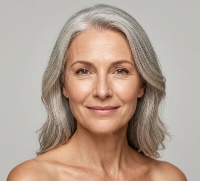 Studio headshot of a senior female model looking at the camera with a gentle smile, aging gracefully and wellness concept