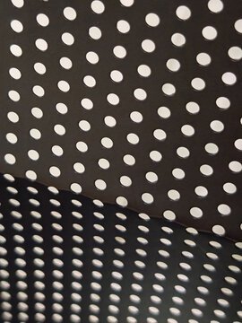 Macro abstract texture of an angled dark perforated surface with bright circular holes and a distinct shadow fold. Suitable as a seamless background for modern industrial design templates, technology 