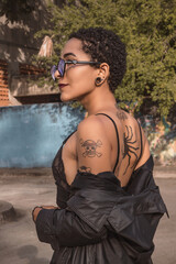 Side profile portrait of young tattooed Latina woman wearing sunglasses outdoors. © Ronald