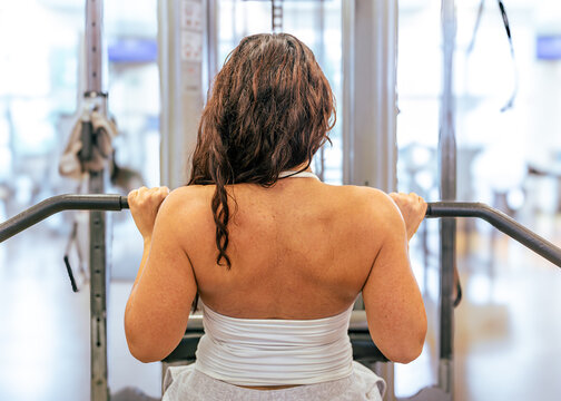 Woman training back muscles doing lat pulldown exercise in gym