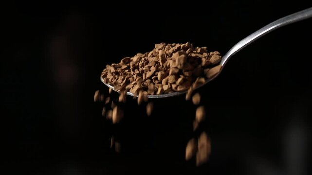 Instant Coffee Granules Falling from Spoon on Black Background