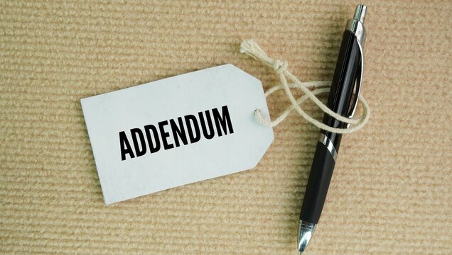 Pen and paper tag with the words Addendum - An added section of information in a letter or report. extra piece of information or a new term added to the end of a completed document, book, or contract.