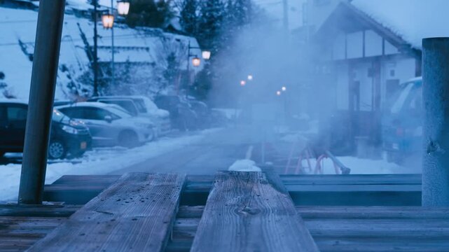 ブルーアワーに湯けむりが立ち込める雪の温泉街の夕暮れ時のスローモーション