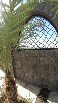 Distant view of Masjid Quba seen through a stone arch window in a sunny courtyard.