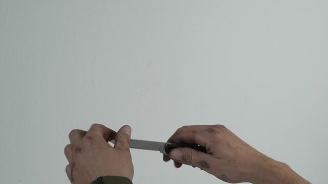 Dirty Hands Closing a Folding Pocket Knife Against a Plain Background