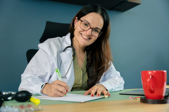Smiling doctor writing medical notes at clinic desk