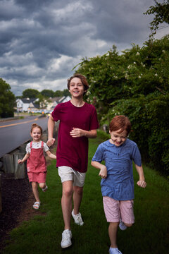 Happy children running together in summer rain under dramatic stormy sky