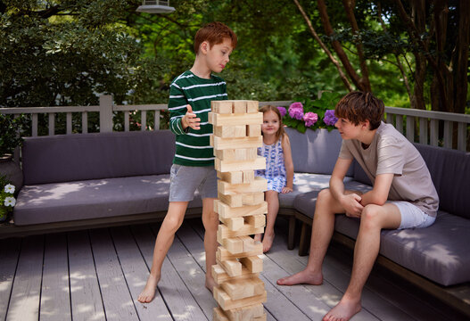 Children playing giant wooden block stacking game together outdoors, at home