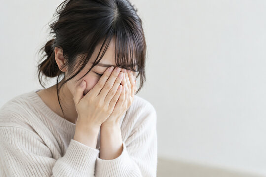 白背景で顔を覆って泣く若い女性