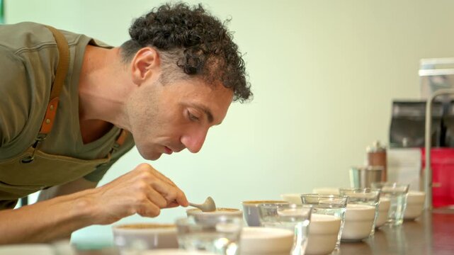 Coffee professional carefully tasting brewed coffee samples during a sensory cupping session, using a spoon to evaluate flavor and quality across multiple cups