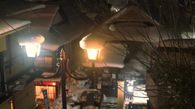 レトロな街灯の温かい明かりが灯る雪降る夜の温泉街のスローモーション
