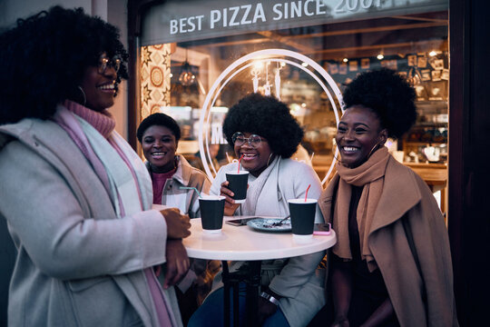 four happy female friends laughing, having fun, socializing at outdoor cafe, dressed for autumn or winter weather.