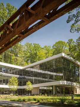 Cantilevered Glass Building Beneath Rusted Steel Truss Bridge on Wooded Campus
