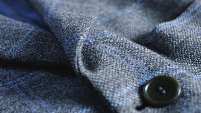 A close-up of a grey-blue tweed woolen jacket lapel highlights fine lining material, elegant buttons, professional tailoring techniques, suiting material texture, and fashion details.