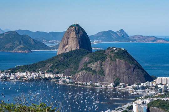 The sweeping view of Sugarloaf Mountain highlights its imposing shape rising above Guanabara Bay, featuring green slopes, blue waters, and the sprawling city. Rio de Janeiro, Brazil.	

