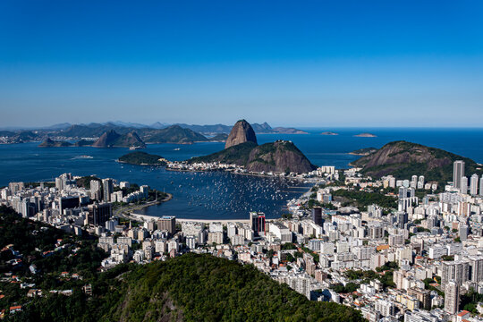 The sweeping view of Sugarloaf Mountain highlights its imposing shape rising above Guanabara Bay, featuring green slopes, blue waters, and the sprawling city. Rio de Janeiro, Brazil.	
