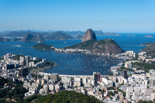 The sweeping view of Sugarloaf Mountain highlights its imposing shape rising above Guanabara Bay, featuring green slopes, blue waters, and the sprawling city. Rio de Janeiro, Brazil.	
