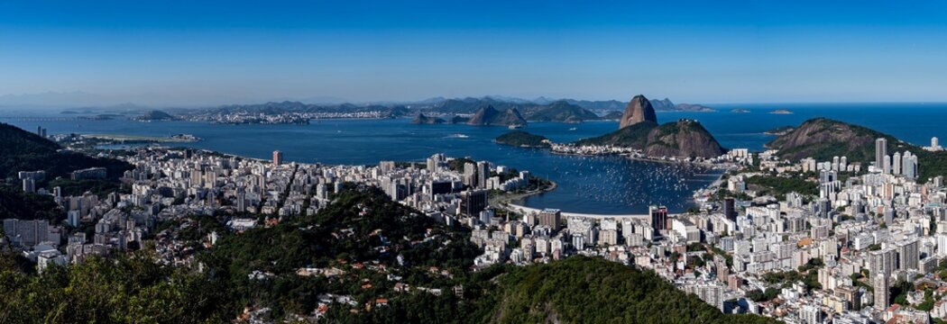 The sweeping view of Sugarloaf Mountain highlights its imposing shape rising above Guanabara Bay, featuring green slopes, blue waters, and the sprawling city. Rio de Janeiro, Brazil.	
