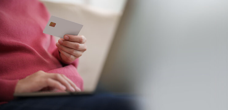 Woman holding a credit card while shopping online on a laptop at home, representing digital payment, e-commerce, cashless transactions, secure checkout and convenient online purchasing.