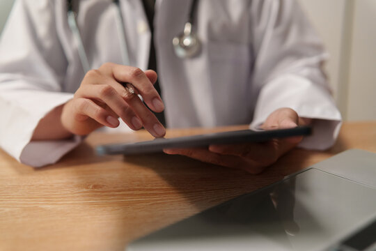 Doctor using digital tablet at a desk, representing medical diagnosis, patient care, healthcare technology, clinical review, digital records and modern medical work.