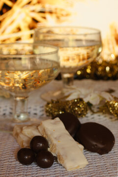 Champagne glasses clinking, celebrating New Year's Eve, Christmas, or holidays with delicious chocolate covered almonds and traditional nougat sweets on a festive table
