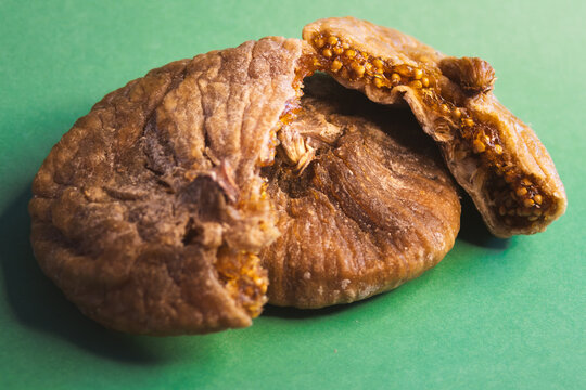 Dried figs with one cut open revealing the seeds and texture, showcasing healthy eating, natural snack options, and Mediterranean dessert ingredients on a green background