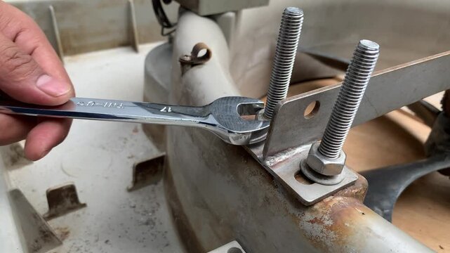 technician hand loosening a nut on a threaded rod using a spanner