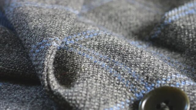 A close-up of a grey tweed woolen jacket lapel showing its elegant finish, smooth dark striped lining under the check pattern fabric, buttons, tailoring technique, and fabric texture.
