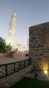 Illuminated minaret and historic stone arches of Masjid Al Fath in Medina at dusk.