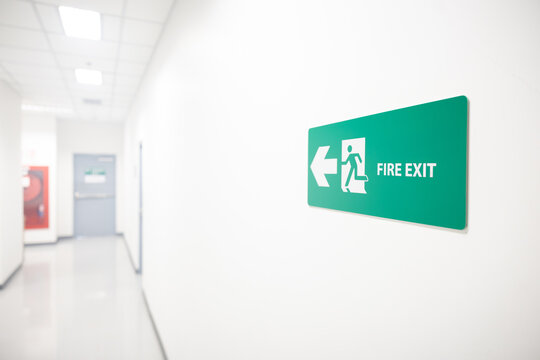Green fire exit sign pointing left in a white hallway