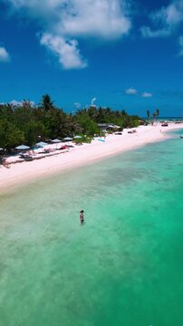 Aerial beach view woman bikini sunbathing relaxed model lies on golden sand under bright sun, turquoise ocean waves lap shoreline, drone captures top down panorama, warm summer,Maldives,vertical video